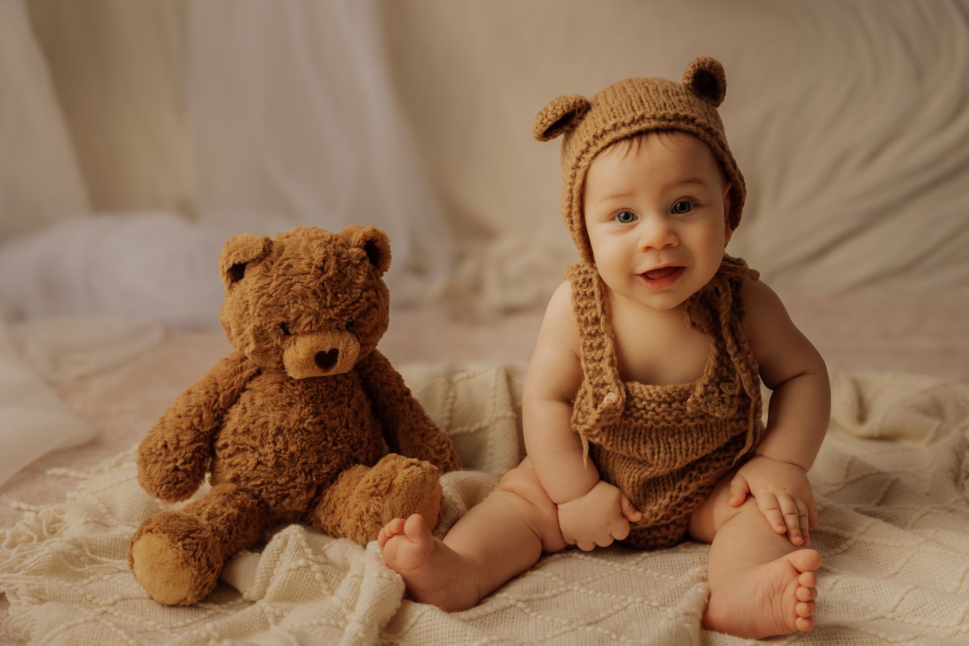 Bambino con cuffietta a orecchie d'orso e salopette di lana seduto accanto a un grande peluche marrone