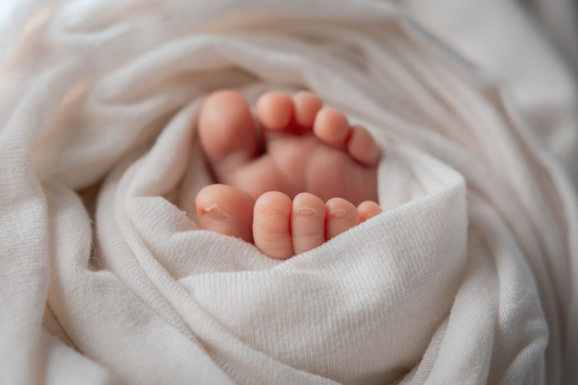 Dettaglio ravvicinato dei piedini del neonato che escono da una copertina bianca