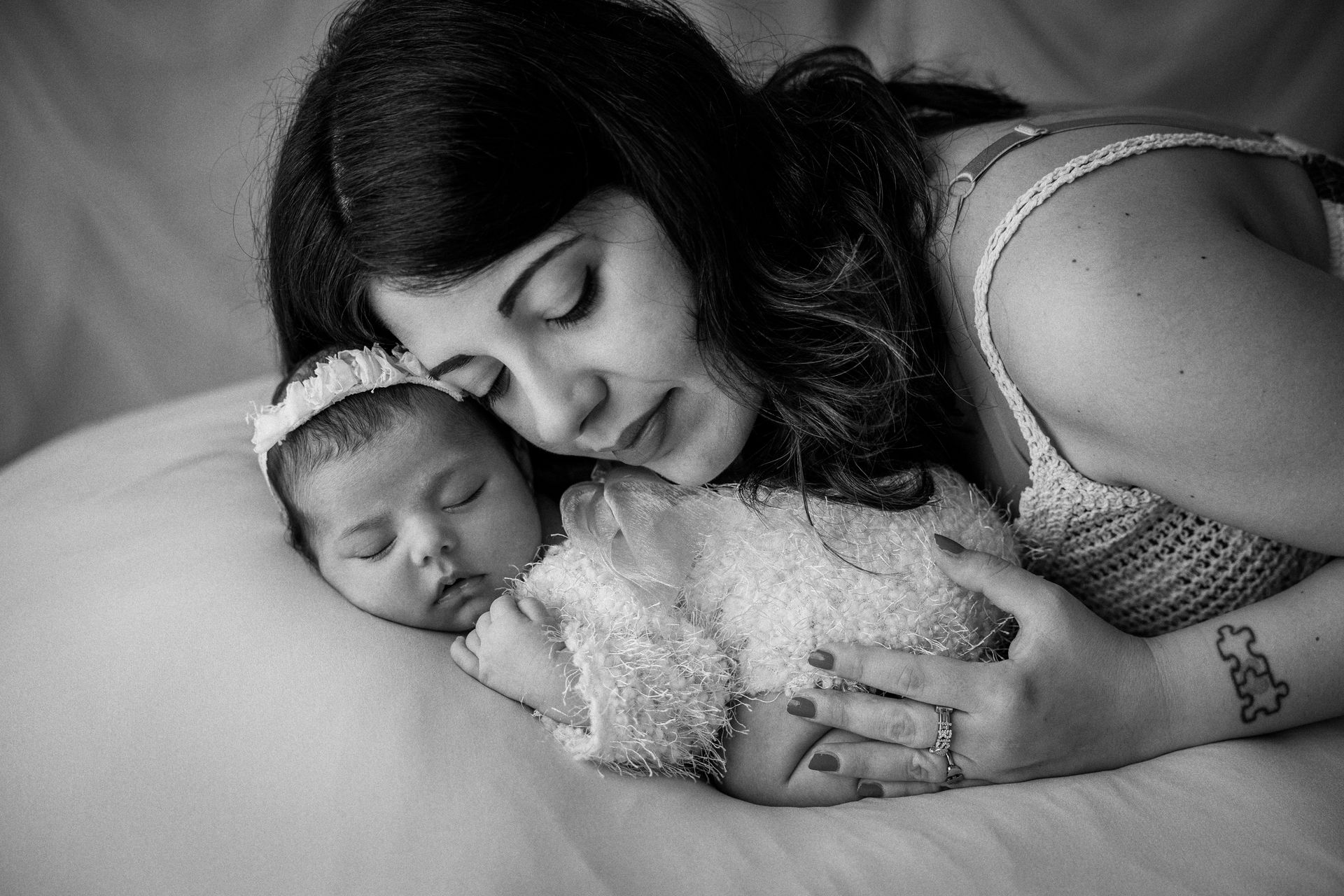 Mamma sdraiata sul letto appoggia la guancia alla neonata addormentata, ritratto in bianco e nero