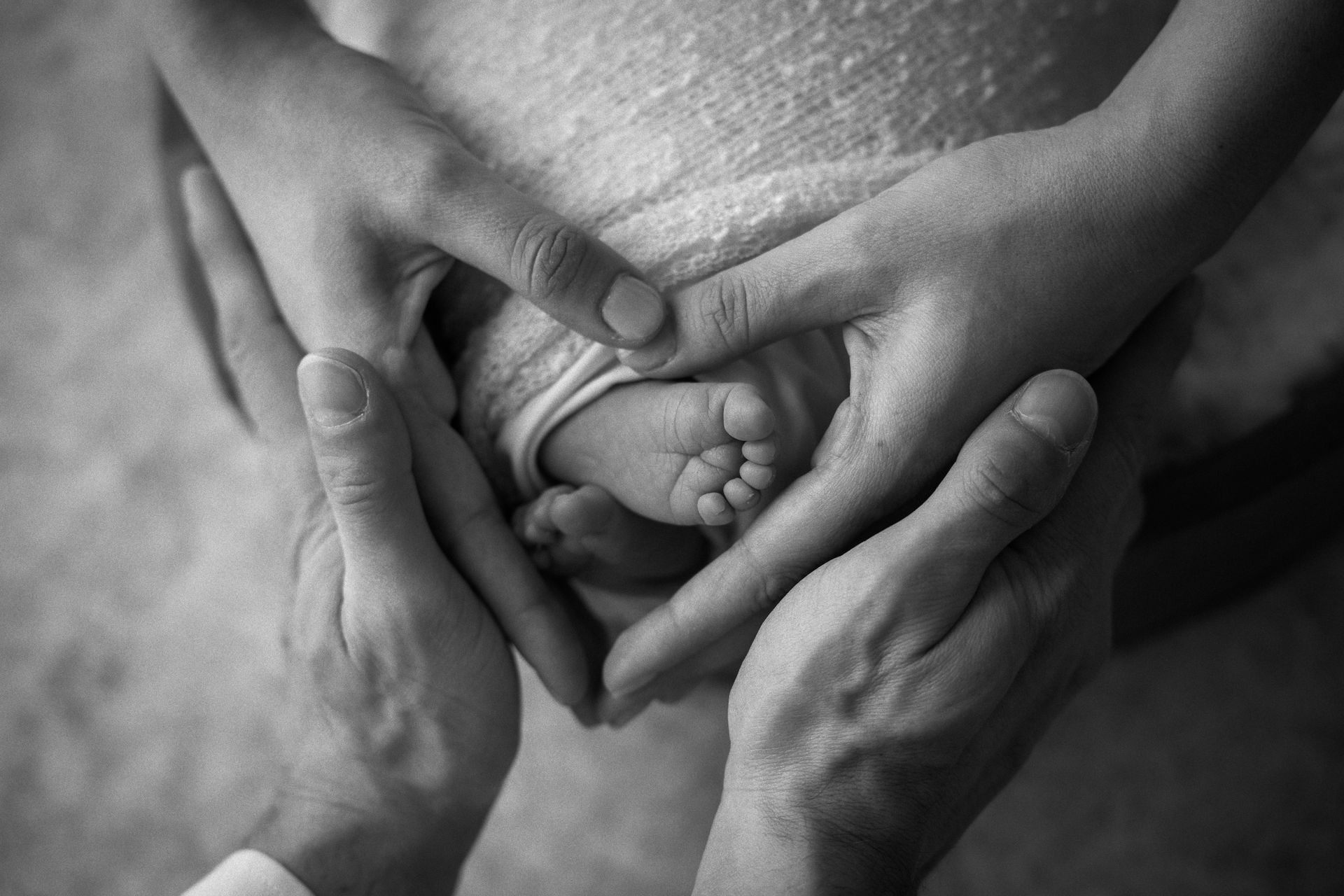 Le mani di mamma e papà formano un cuore attorno ai piedini del neonato, dettaglio in bianco e nero