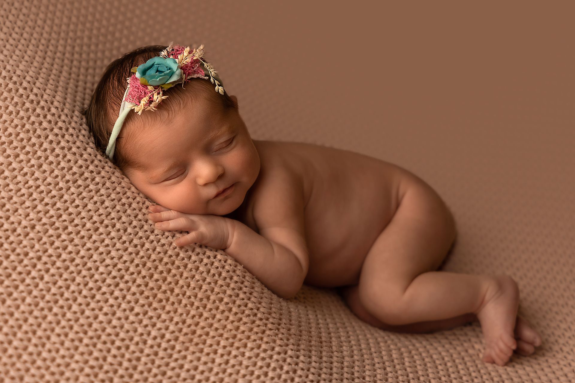 Neonata con corona di fiori riposa a pancia in giù su una coperta marrone lavorata