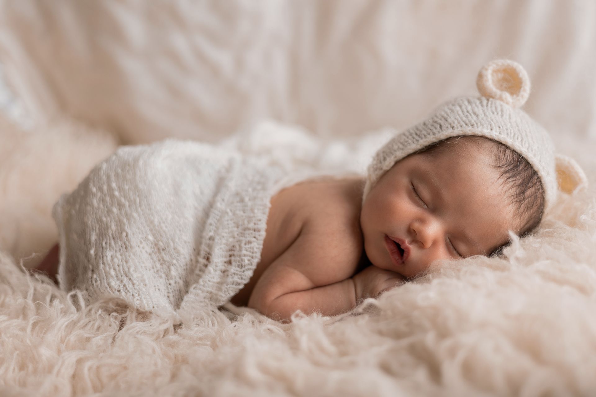 Bimbo con cappellino a orecchie d'orso dorme a pancia in giù sul pelo lungo crema