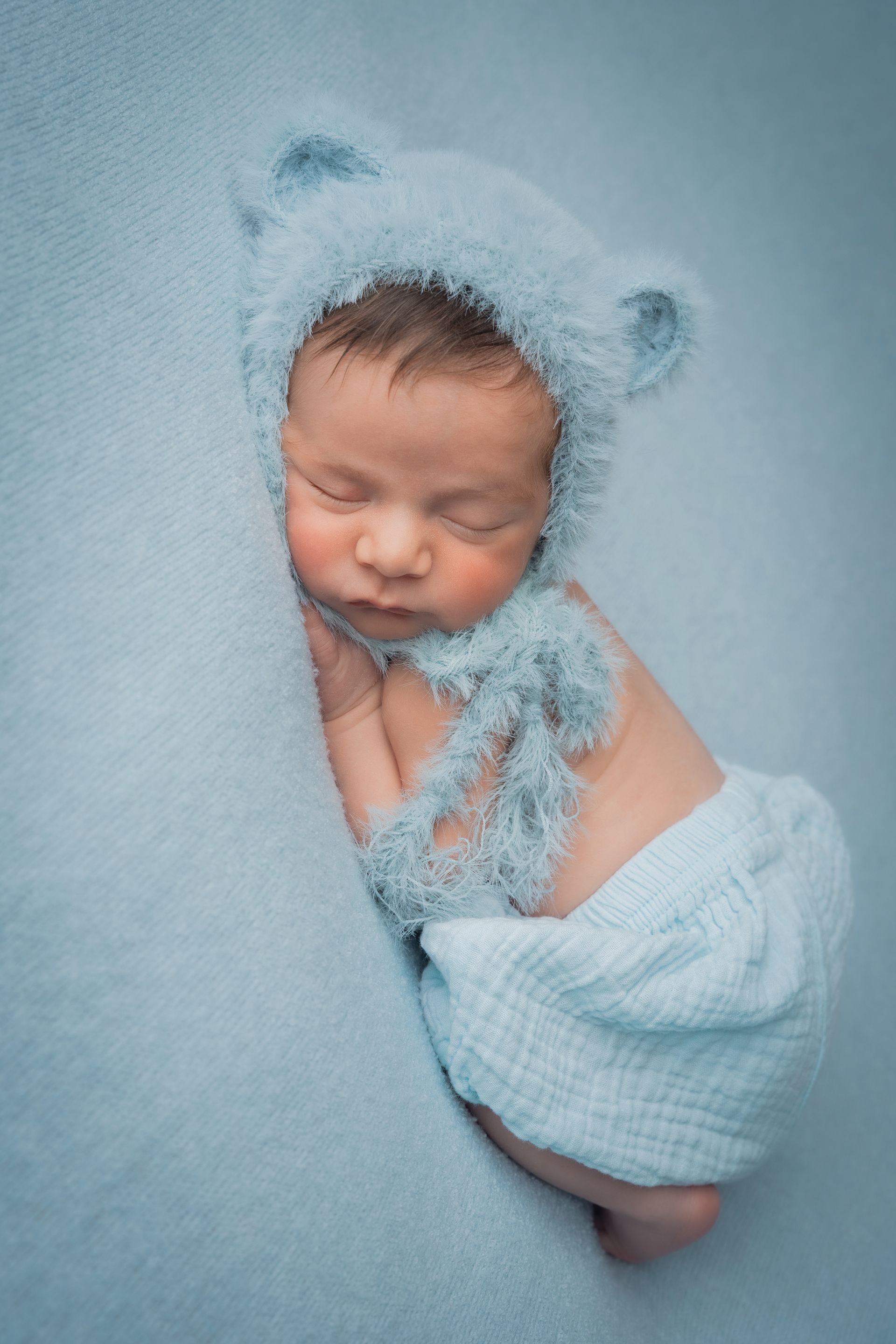 Neonato con la cuffietta azzurra a orecchie d'orso dorme raccolto su un fondo azzurro