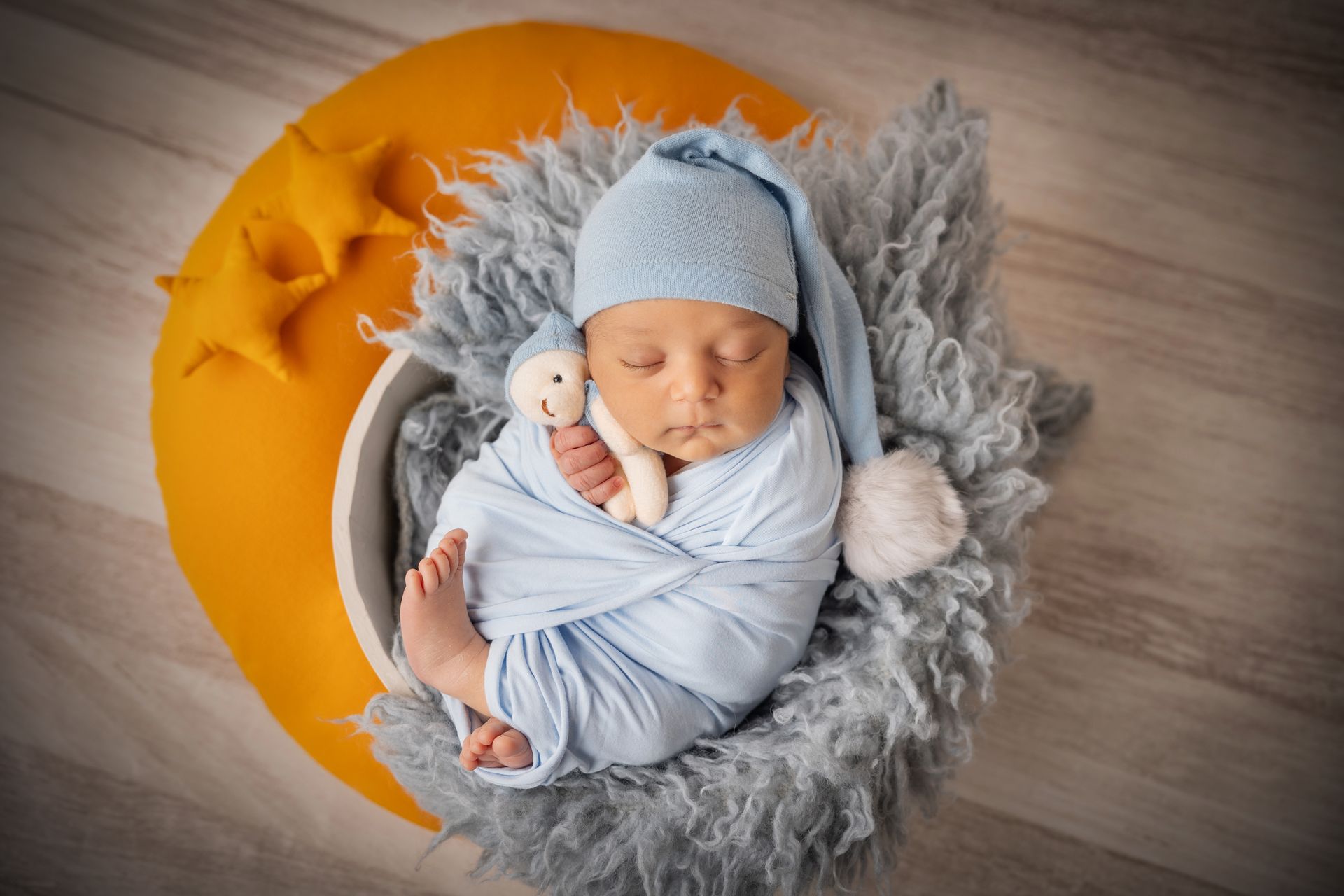 Neonato fasciato in azzurro con cappellino dorme in un cesto di pelliccia grigia appoggiato su una luna gialla