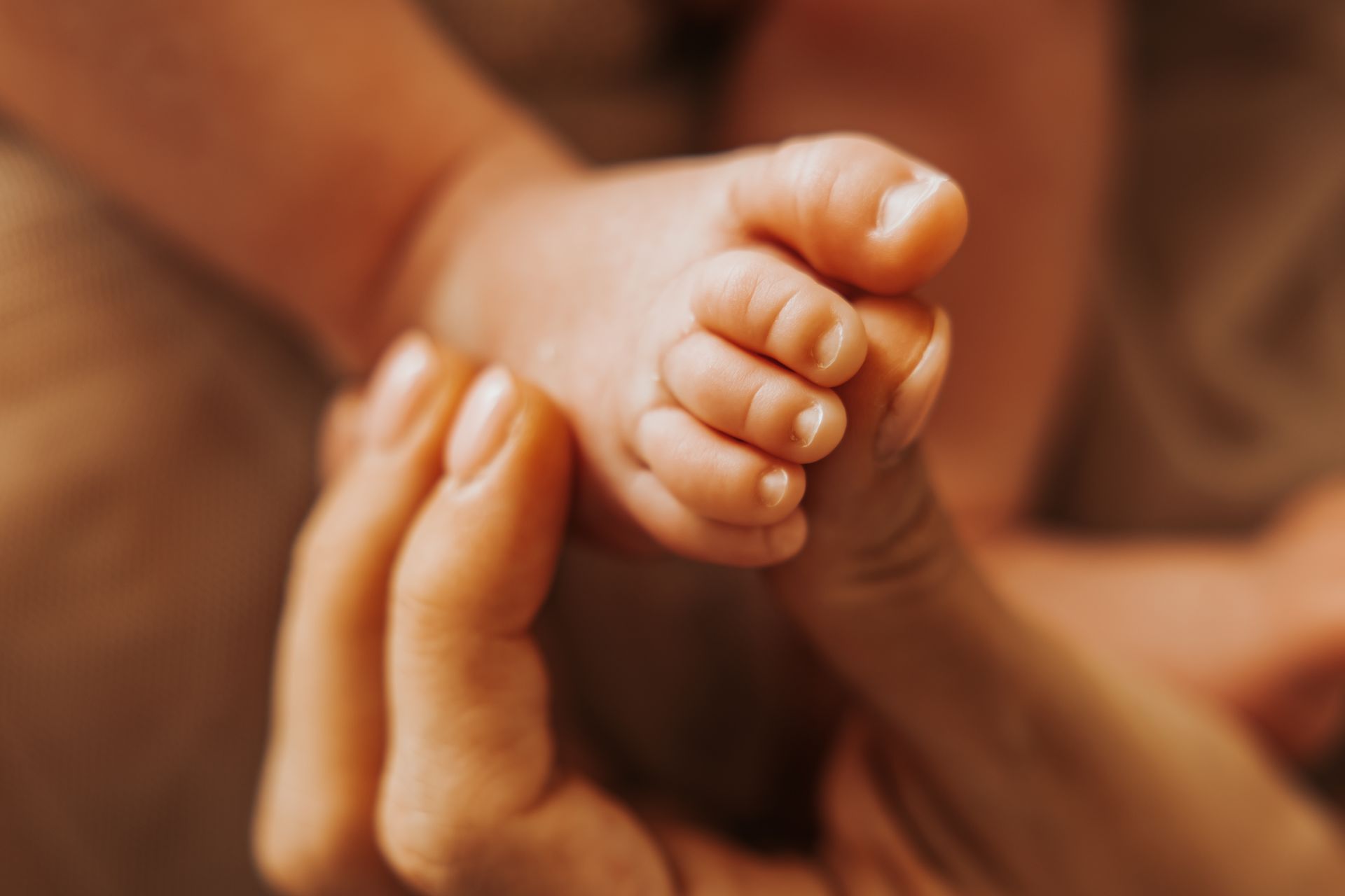 Piedini di un neonato sorretti da una mano adulta in una luce calda color ambra