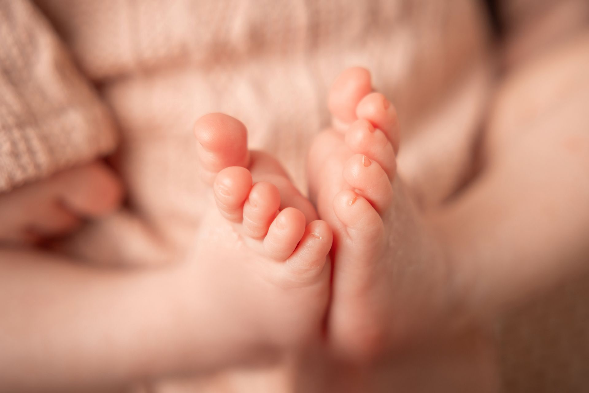 Dettaglio ravvicinato dei piedini rosati di un neonato appoggiati sul palmo di una mano adulta